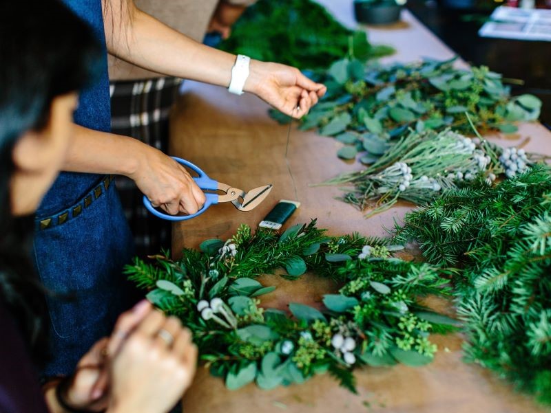 Table showing green wreaths being made by two people to the side