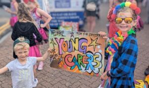 Two children in colourful clothes holding up a graffiti sign that says 'Young Carers'.