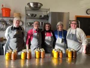 Five carers wearing aprons with full jars on the kitchen unit in front of them.