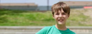 A young boy in a green tshirt, outside, facing the camera.